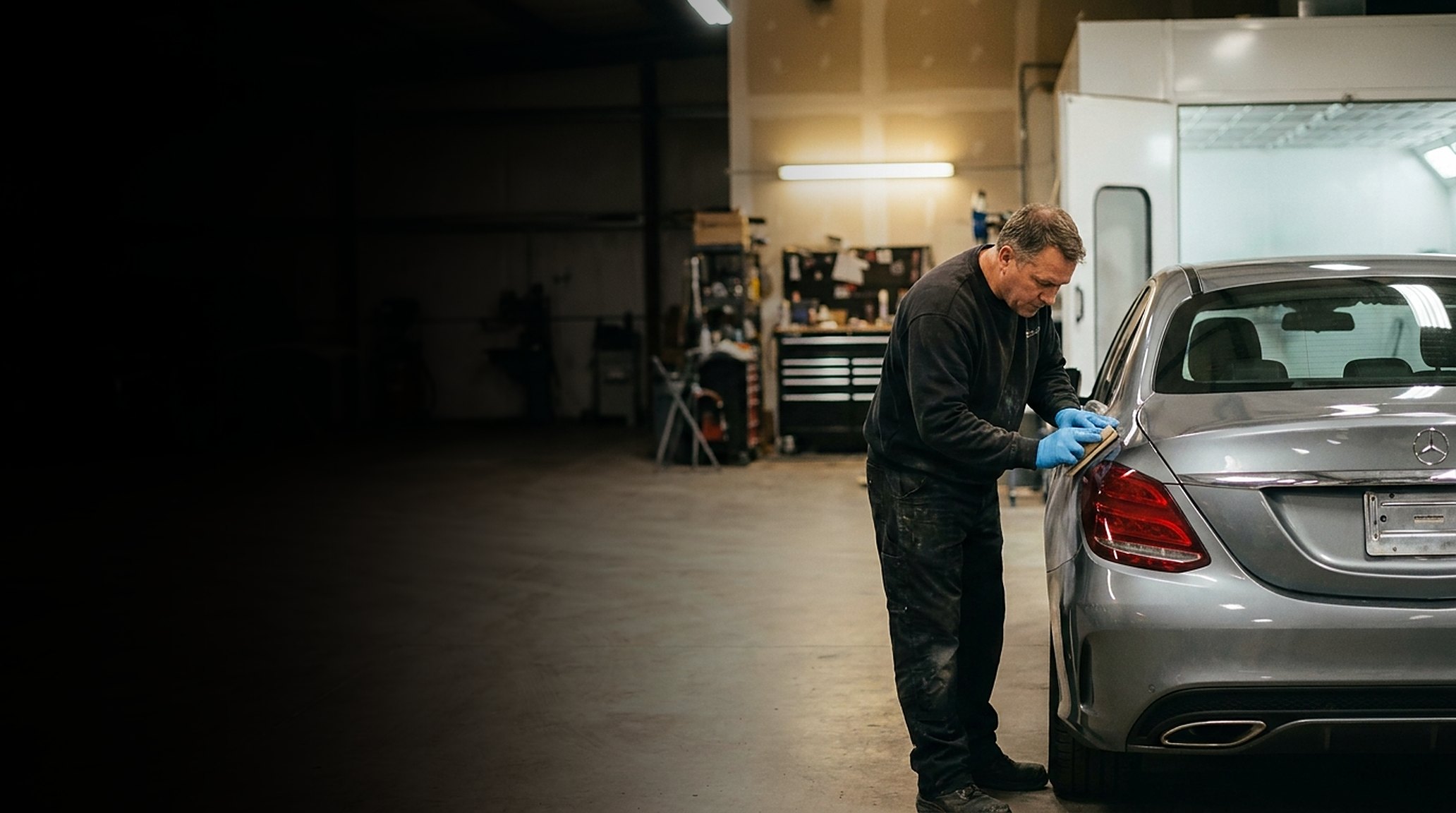 A body technician block-sanding the repaired rear quarter of a silver Mercedes-Benz C-Class in the shop